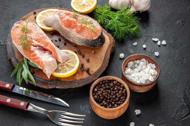 Vista frontale fette di pesce fresco con fette di limone e aglio su colore scuro cibo carne pesce oscurità piatto foto