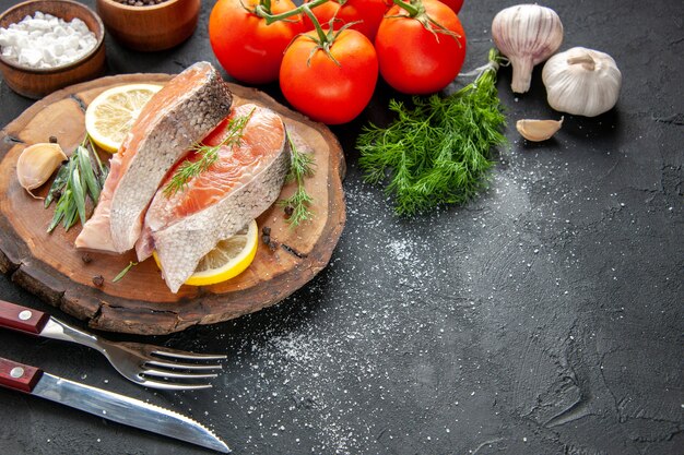 Vista frontale fette di pesce fresco con fette di limone e pomodori su carne di colore scuro piatto di pesce foto cibo crudo