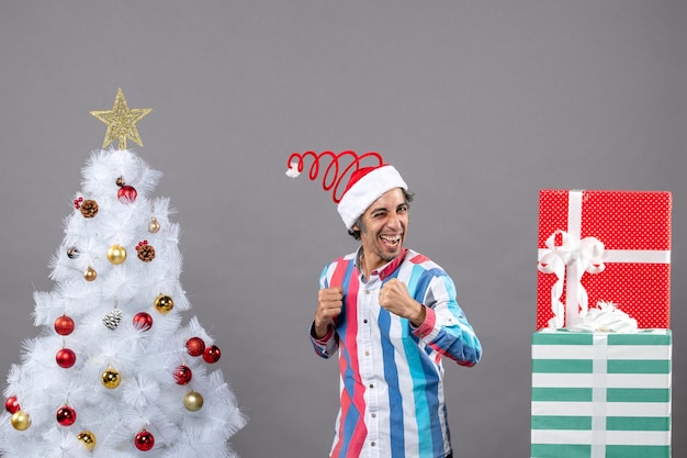 Vista frontale fiducioso uomo felice in piedi vicino all'albero di Natale bianco