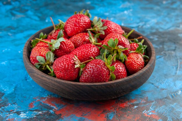 Vista frontale fragole rosse fresche all'interno del piatto su sfondo blu vitamina colore frutti di bosco