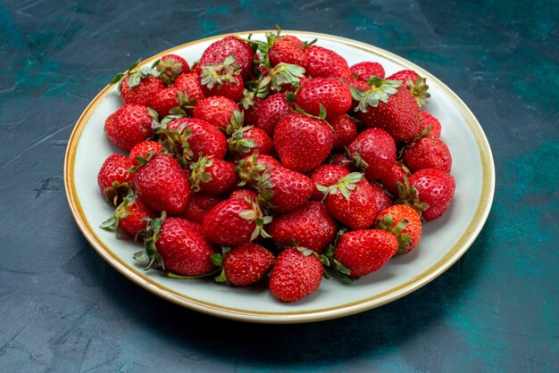 Vista frontale fragole rosse fresche mellow frutti di bosco all'interno della piastra sulla superficie blu scuro frutti di bosco mellow summer