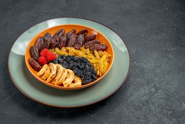 Vista frontale frutta secca con uvetta all'interno del piatto su uno spazio grigio scuro