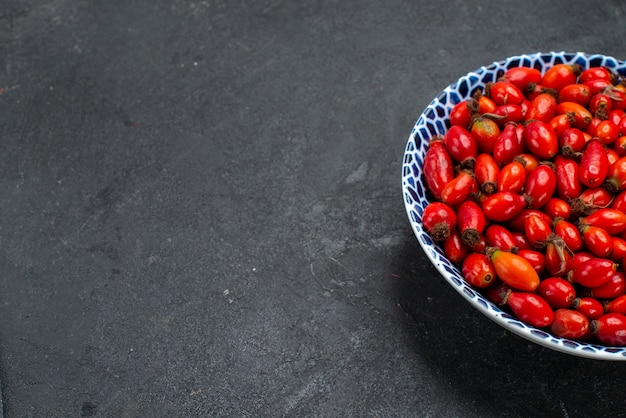 Vista frontale frutti rossi maturi e bacche acide all'interno della piastra sulla superficie grigia frutti berry color vitamina pianta ad albero