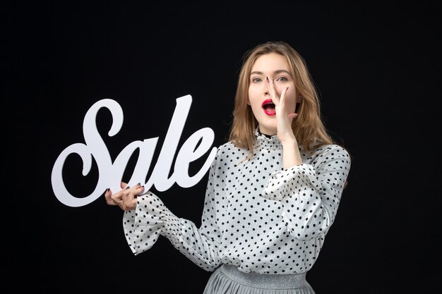 Vista frontale giovane bella donna che tiene vendita scrivendo sulla parete nera colore shopping modello moda foto emozione