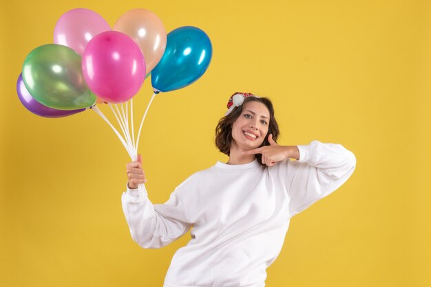 Vista frontale giovane bella femmina azienda palloncini su colore giallo Natale donna capodanno emozione