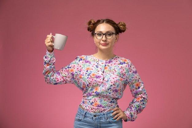 Vista frontale giovane bella femmina in camicia fiore progettato e blue jeans che tengono una tazza sui precedenti rosa