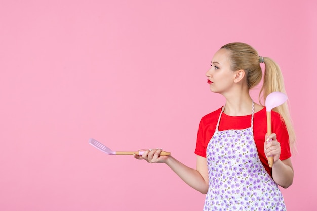 Vista frontale giovane casalinga che tiene le posate sulla parete rosa