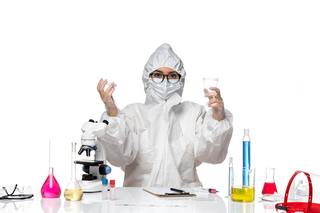 Vista frontale giovane chimico femminile in speciale tuta protettiva tenendo il pallone con la soluzione e la scrittura su sfondo bianco laboratorio covid chimica virus