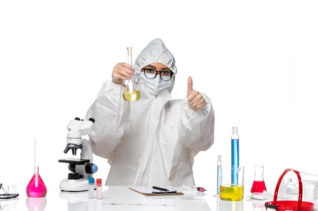 Vista frontale giovane chimico femminile in speciale tuta protettiva tenendo il pallone con soluzione su sfondo bianco chiaro laboratorio covid chimica virus