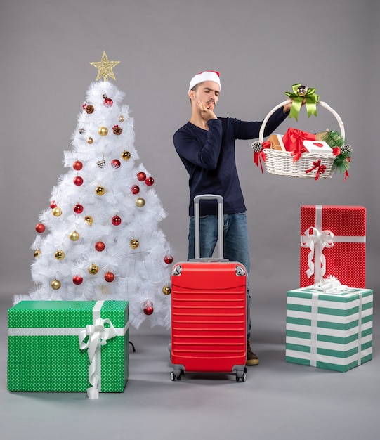 Vista frontale giovane con cappello da Babbo Natale guardando cesto regalo facendo segno bacio chef italiano su grigio isolato