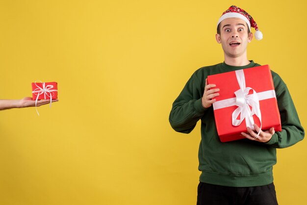 Vista frontale giovane con gli occhi spalancati che tiene il regalo di natale il regalo in mano femminile su colore giallo