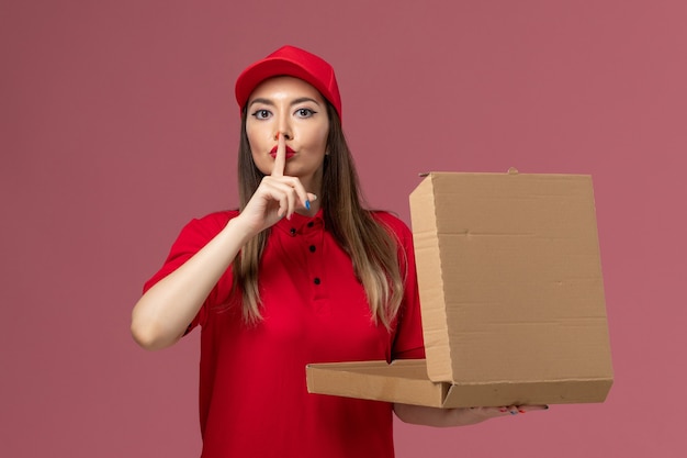 Vista frontale giovane corriere femminile in uniforme rossa che tiene la scatola di cibo di consegna su sfondo rosa chiaro azienda uniforme di lavoro di consegna del servizio