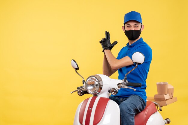 Vista frontale giovane corriere maschio in uniforme blu su sfondo giallo covid-pandemia servizio lavoro virus consegna del lavoro bici