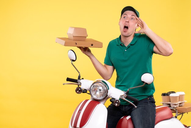 Vista frontale giovane corriere maschio in uniforme che tiene in mano confezioni di cibo su giallo