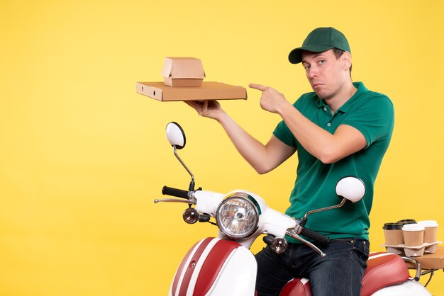 Vista frontale giovane corriere maschio in uniforme che tiene in mano confezioni di cibo su giallo