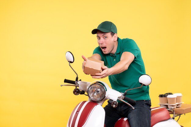 Vista frontale giovane corriere maschio in uniforme che tiene un piccolo pacchetto di cibo su giallo