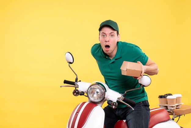 Vista frontale giovane corriere maschio in uniforme che tiene un piccolo pacchetto di cibo su giallo