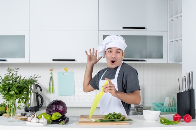 Vista frontale giovane cuoco in uniforme che mostra il suo nuovo armadio da cucina