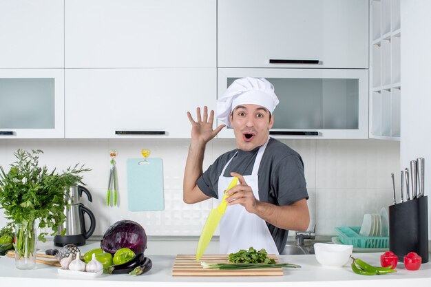 Vista frontale giovane cuoco in uniforme che mostra il suo nuovo armadio da cucina