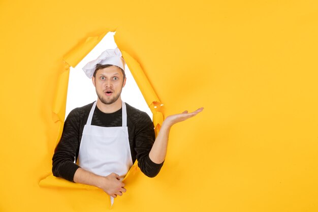 Vista frontale giovane cuoco maschio in mantello bianco e berretto su sfondo giallo strappato cibo lavoro cucina bianca uomo cucina foto colore