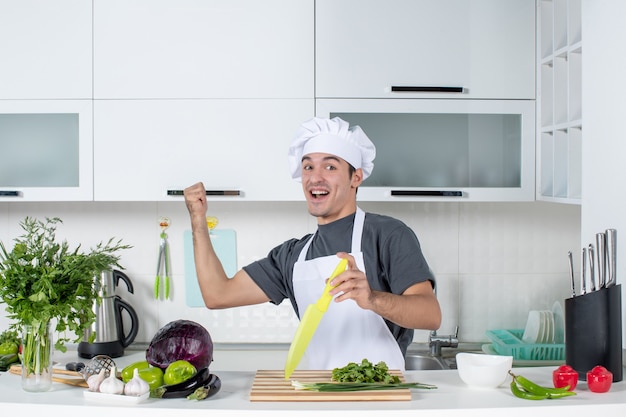 Vista frontale giovane cuoco molto felice in uniforme che punta all'armadio