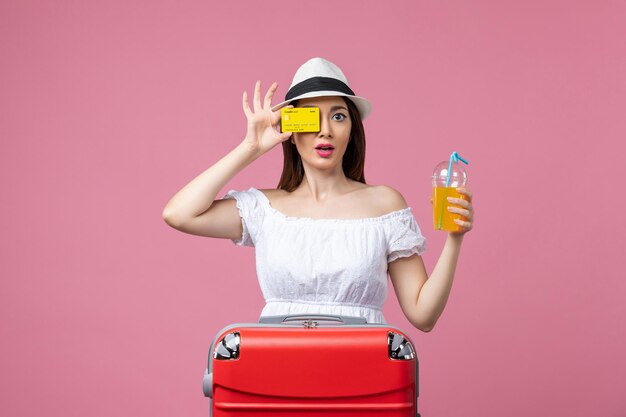 Vista frontale giovane donna che tiene bevanda e carta di credito sul muro rosa viaggio vacanza estate viaggio colori di calore