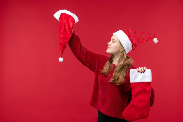 Vista frontale giovane donna che tiene calzino e berretto rossi grandi, vacanze natale rosso