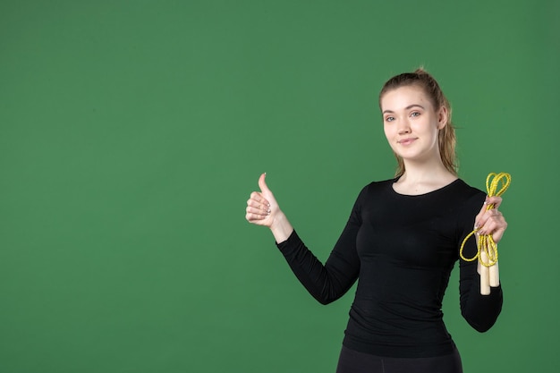 Vista frontale giovane donna che tiene la corda per saltare su sfondo verde donna allenamento colori sport atleta corpo ginnastica salute