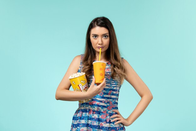 Vista frontale giovane donna che tiene popcorn e bevanda sulla superficie blu