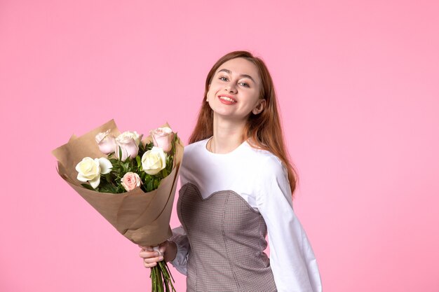 Vista frontale giovane donna che tiene un mazzo di belle rose sul rosa