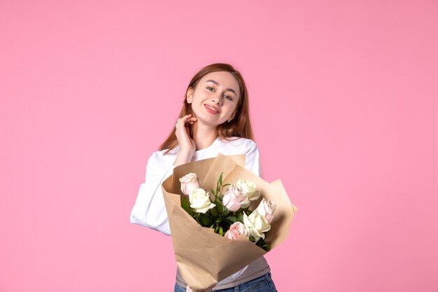 Vista frontale giovane donna che tiene un mazzo di belle rose sul rosa