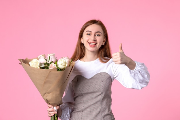 Vista frontale giovane donna che tiene un mazzo di bellissime rose che mostrano un gesto fantastico sul rosa