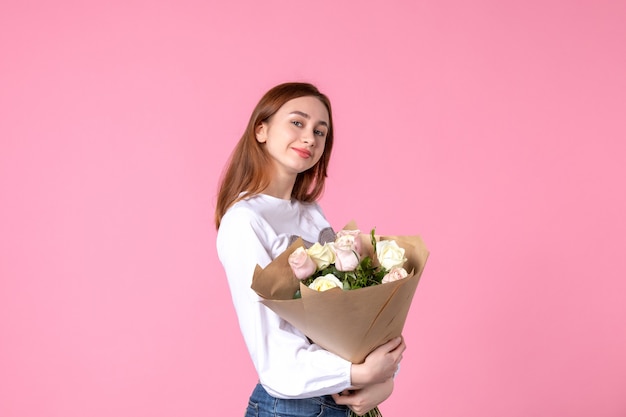 Vista frontale giovane donna che tiene un mazzo di bellissime rose su rosa