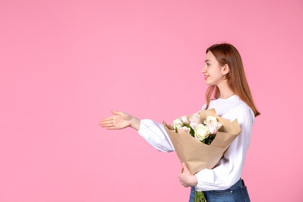 Vista frontale giovane donna che tiene un mazzo di bellissime rose su rosa