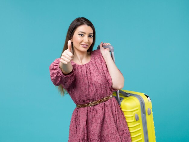 Vista frontale giovane donna che va in vacanza con la sua borsa gialla sorridente su sfondo blu viaggio estate viaggio donna mare umano