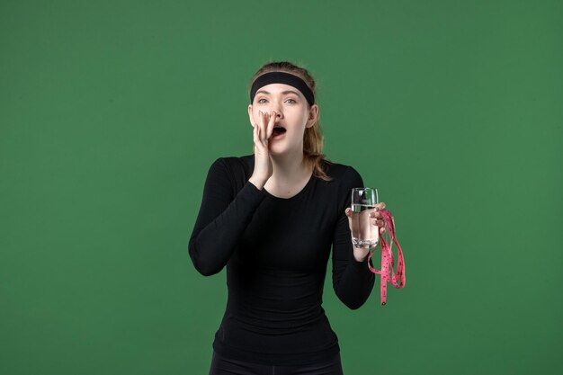 Vista frontale giovane donna con bicchiere d'acqua e misura della vita su sfondo verde salute sport atleta corpo allenamento nero colore donna