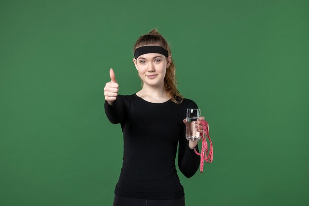 Vista frontale giovane donna con bicchiere d'acqua e misura della vita su sfondo verde sport atleta donna colore del corpo salute allenamento nero