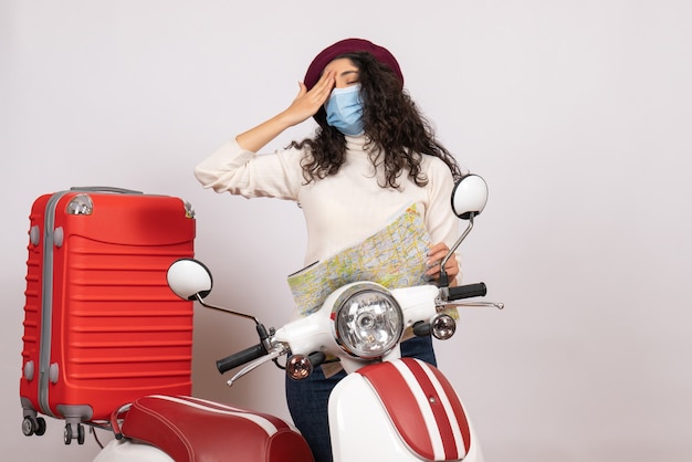 Vista frontale giovane donna con bici in maschera che tiene mappa sullo sfondo bianco colore virus velocità covid-motocicletta veicolo pandemico