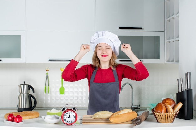 Vista frontale giovane donna con cappello da cuoco e grembiule che mostra la sua felicità in cucina