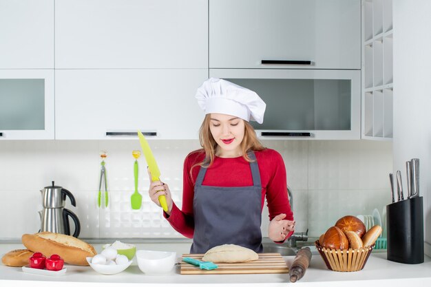 Vista frontale giovane donna con cappello da cuoco e grembiule che tiene un coltello verde in cucina