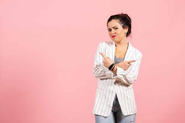 Vista frontale giovane donna con giacca bianca in posa su sfondo rosa chiaro moda donna emozioni colore sensazione lady