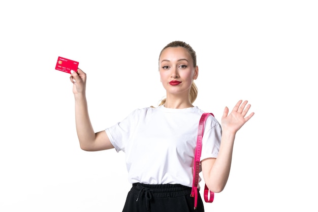 Vista frontale giovane donna con metro a nastro e carta di credito su superficie bianca