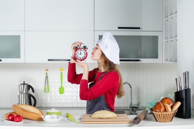 Vista frontale giovane donna con sveglia rossa in cucina in