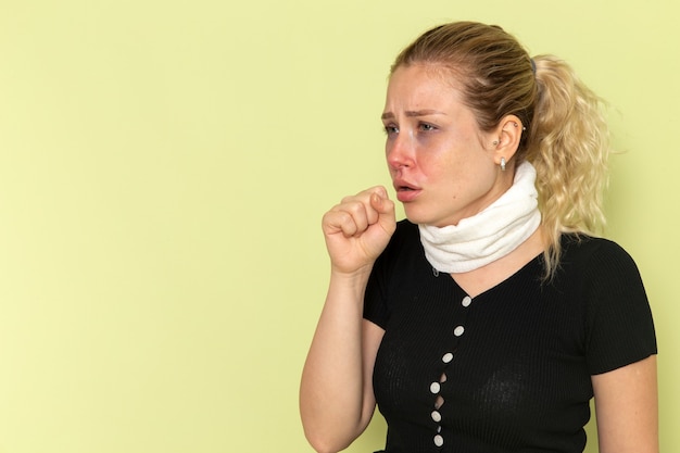 Vista frontale giovane donna con un asciugamano bianco intorno alla gola sensazione di malessere e tosse malata sul muro verde malattia malattia colore femminile salute