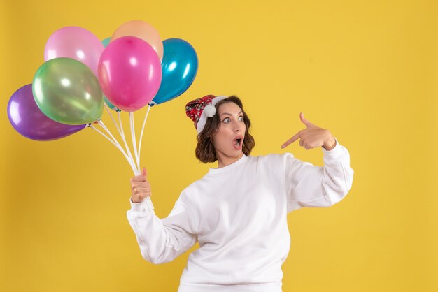 Vista frontale giovane donna graziosa che tiene palloncini colorati sul colore giallo della donna di emozioni natale capodanno