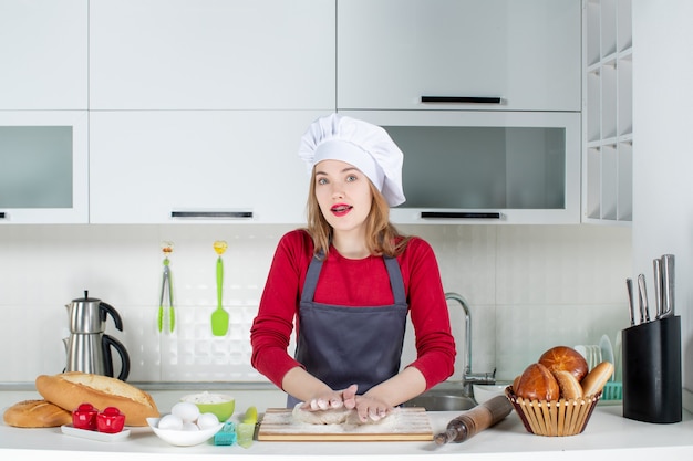 Vista frontale giovane donna impegnata in cappello da cuoco e grembiule che impasta la pasta in cucina