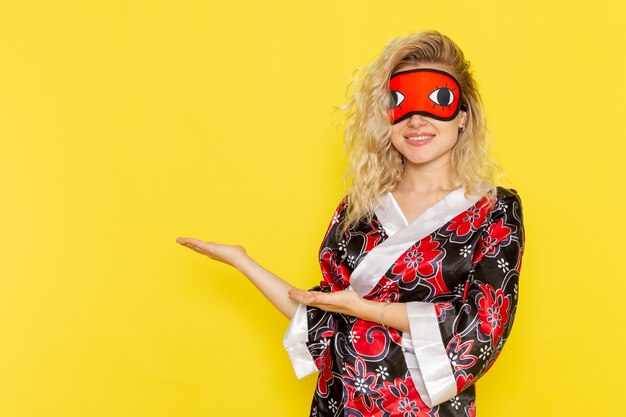 Vista frontale giovane donna in abito da notte e indossa la maschera per gli occhi si prepara a dormire sorridendo sul muro giallo notte sonno oscurità femminile colore