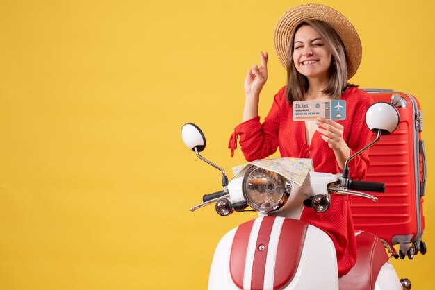 Vista frontale giovane donna in abito rosso con biglietto che fa segno di desiderio sul motorino