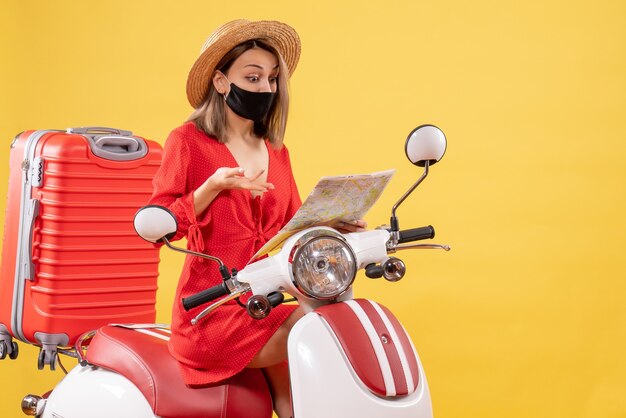 Vista frontale giovane donna in abito rosso sul motorino guardando la mappa