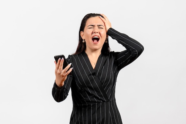 Vista frontale giovane donna in abito scuro rigoroso che tiene il telefono con la faccia dolorosa su uno sfondo bianco donna signora moda lavoro bellezza